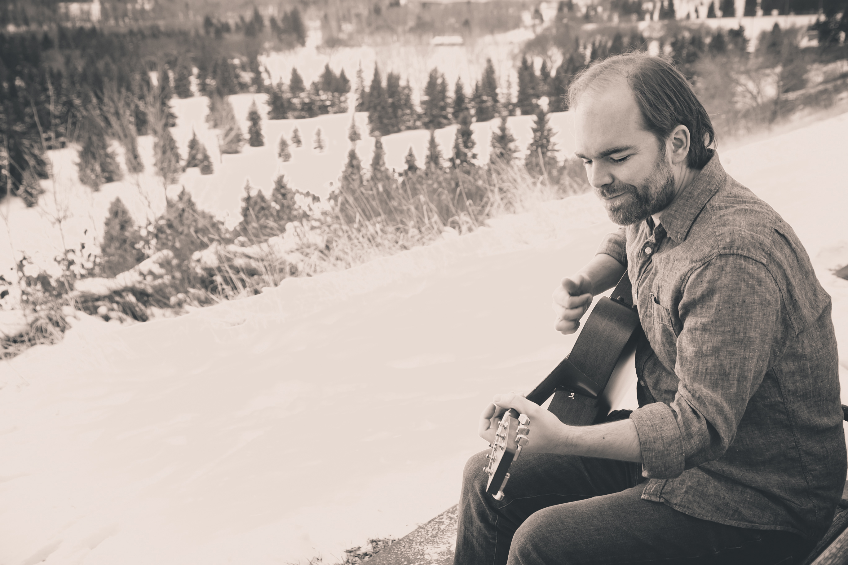 Douglas Mitchell playing acoustic guitar in the winter river valley